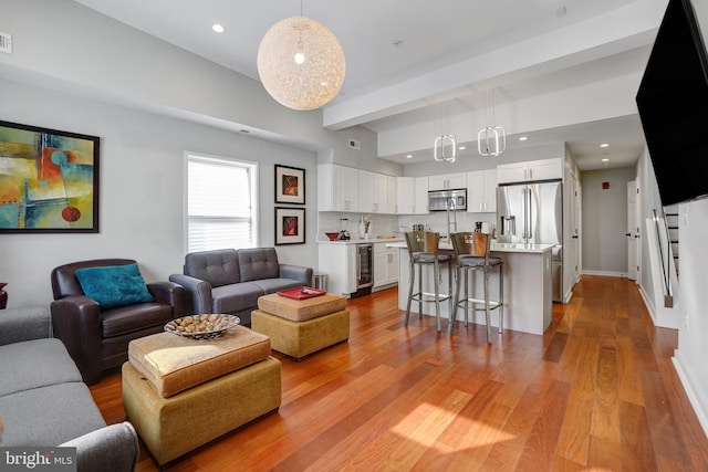 living area featuring beverage cooler, light wood-type flooring, beamed ceiling, recessed lighting, and baseboards