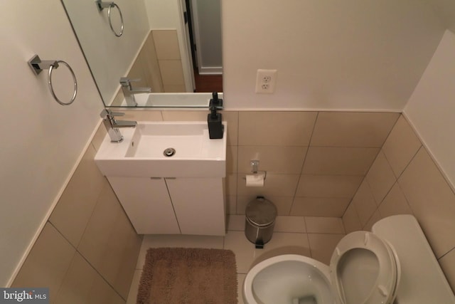 bathroom with tile walls, toilet, wainscoting, and a sink