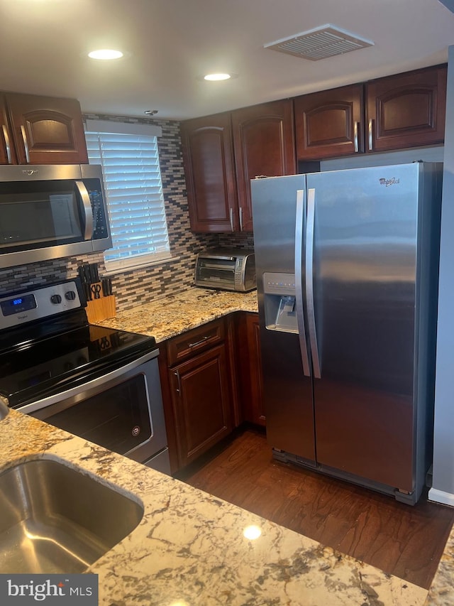 kitchen with appliances with stainless steel finishes, light stone countertops, tasteful backsplash, dark wood-style floors, and recessed lighting