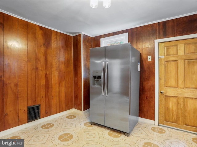 kitchen featuring stainless steel fridge with ice dispenser, wood walls, light tile patterned flooring, and baseboards