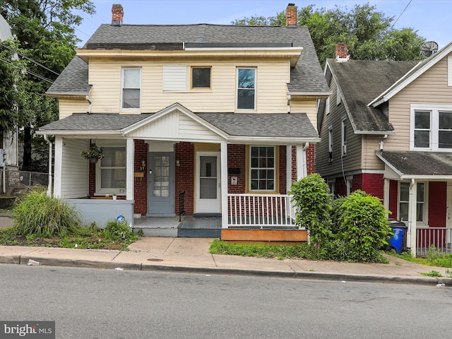 view of front facade with covered porch, brick siding, a chimney, and a shingled roof
