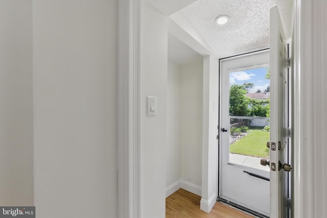 doorway to outside featuring light wood-type flooring, baseboards, and a textured ceiling