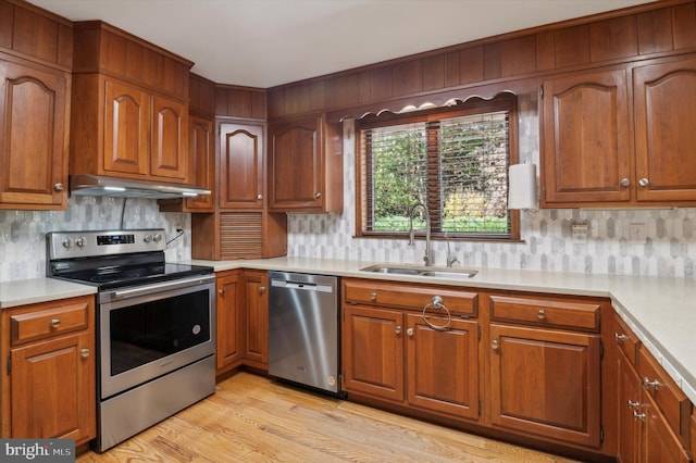 kitchen with appliances with stainless steel finishes, a sink, under cabinet range hood, light countertops, and brown cabinetry