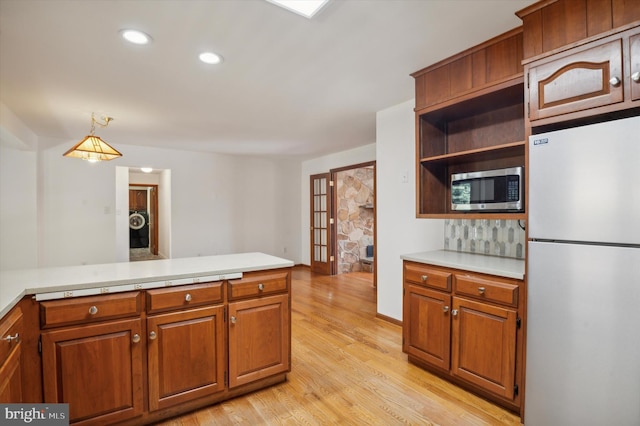 kitchen featuring freestanding refrigerator, stainless steel microwave, light countertops, light wood finished floors, and brown cabinetry