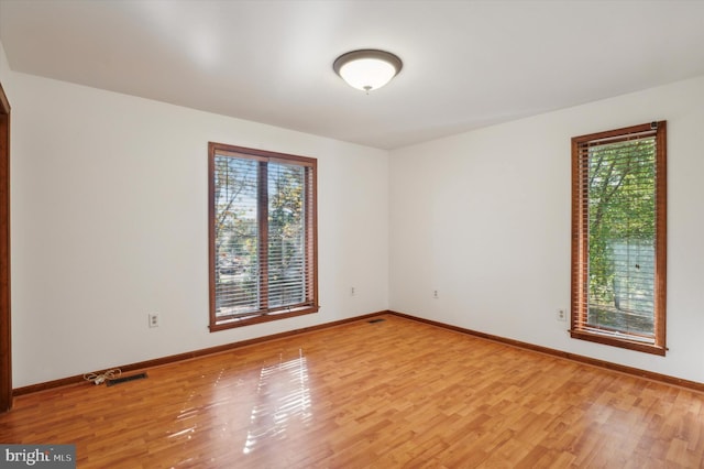 unfurnished room featuring plenty of natural light, light wood-type flooring, and baseboards