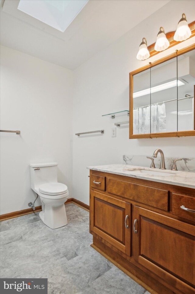 full bath featuring baseboards, toilet, a skylight, and vanity