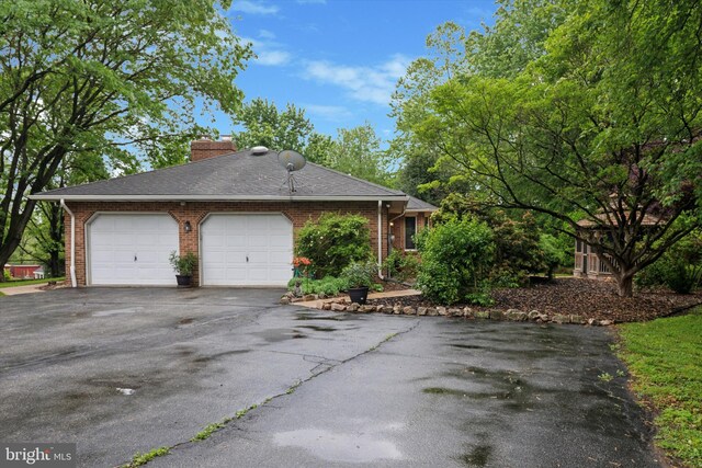 ranch-style home featuring driveway, an attached garage, brick siding, and a chimney