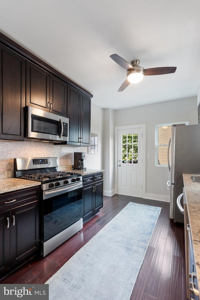 kitchen with stainless steel appliances, decorative backsplash, dark wood-style floors, a ceiling fan, and baseboards