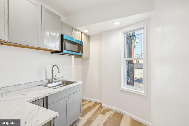 702 Main St, Darby, PA 19023 - kitchen with a sink, stainless steel microwave, light wood finished floors, baseboards, and light stone countertops