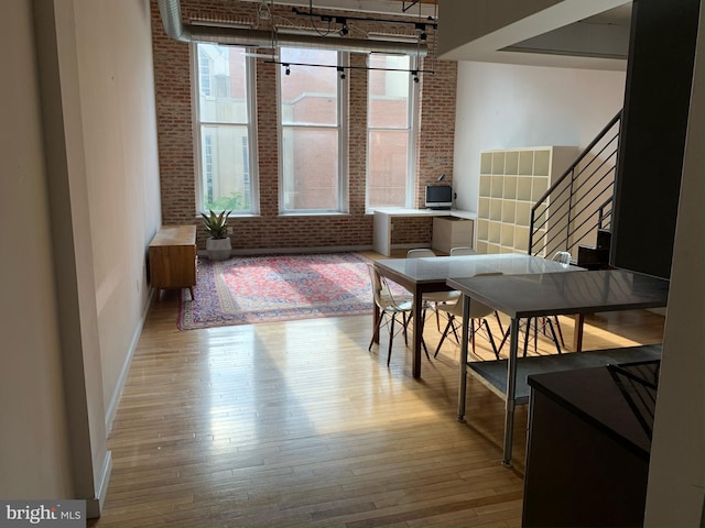 dining room with brick wall, wood-type flooring, baseboards, stairway, and a high ceiling