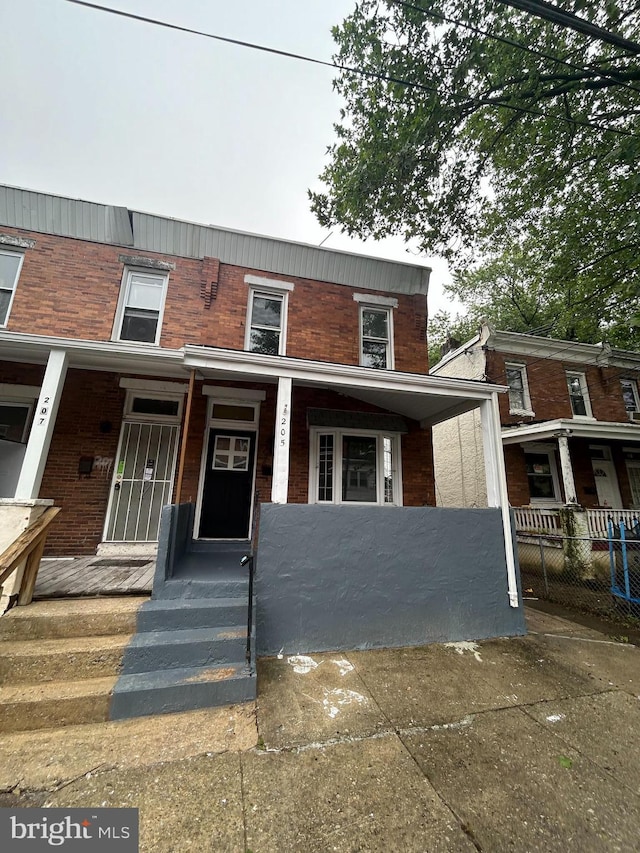 view of front of home with brick siding, a porch, and fence