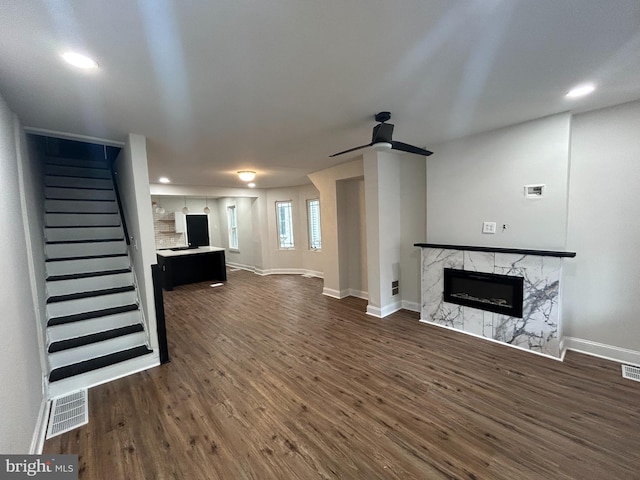 unfurnished living room with a fireplace, a ceiling fan, dark wood-type flooring, stairway, and baseboards
