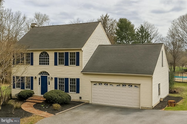 colonial inspired home with a chimney, driveway, and a garage