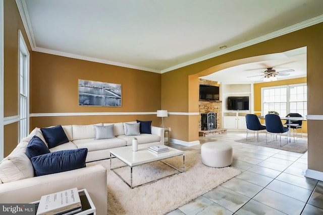 living area featuring tile patterned flooring, crown molding, a fireplace, ceiling fan, and baseboards