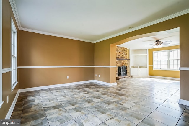 unfurnished living room with ornamental molding, a stone fireplace, baseboards, ceiling fan, and tile patterned floors