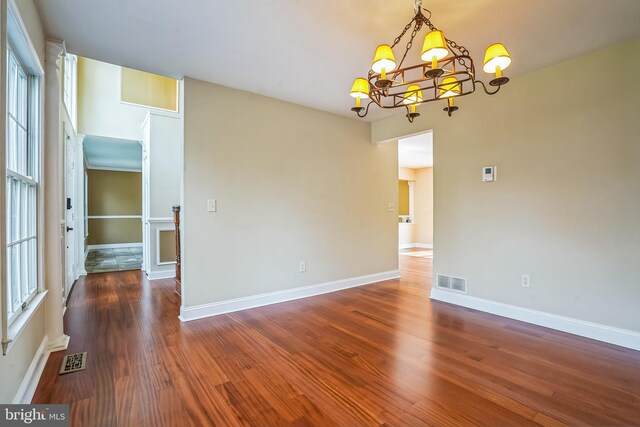 unfurnished room featuring a chandelier, healthy amount of natural light, wood finished floors, and baseboards