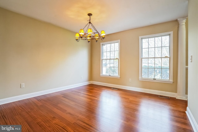 empty room featuring a chandelier, baseboards, wood finished floors, and decorative columns