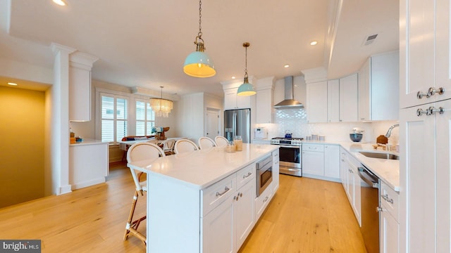 625 Bay Ave, Ocean City, NJ 08226 - kitchen with appliances with stainless steel finishes, wall chimney range hood, a breakfast bar, a sink, and light wood finished floors