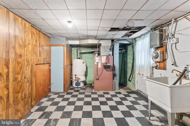 below grade area featuring water heater, dark floors, heating unit, a sink, and wood walls
