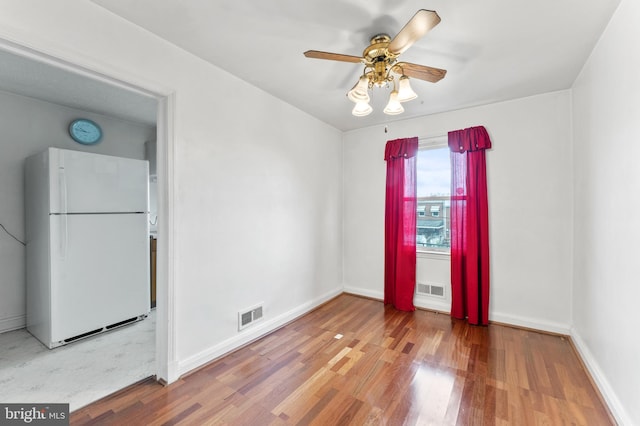 empty room with wood finished floors, a ceiling fan, and baseboards