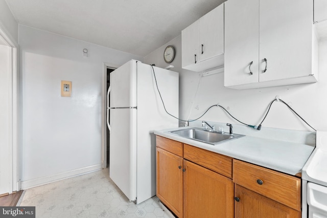 kitchen with freestanding refrigerator, a sink, light countertops, baseboards, and brown cabinetry