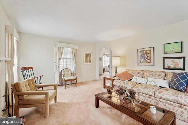 living area featuring arched walkways, light carpet, and baseboards