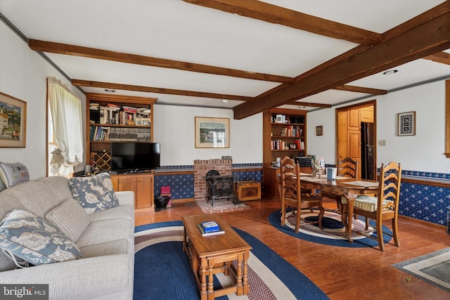 living area featuring wood finished floors, a wood stove, beamed ceiling, wallpapered walls, and built in shelves