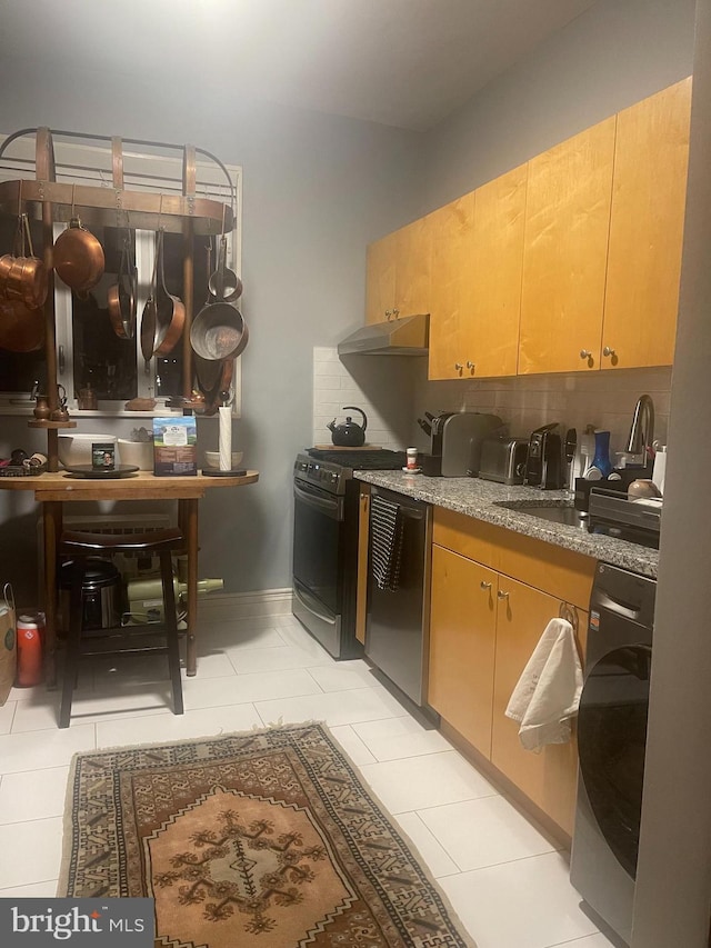 kitchen featuring under cabinet range hood, gas range oven, dishwasher, light tile patterned floors, and stone countertops