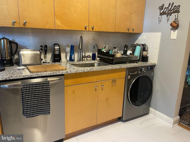 kitchen featuring stainless steel dishwasher, washer / clothes dryer, backsplash, light stone countertops, and baseboards