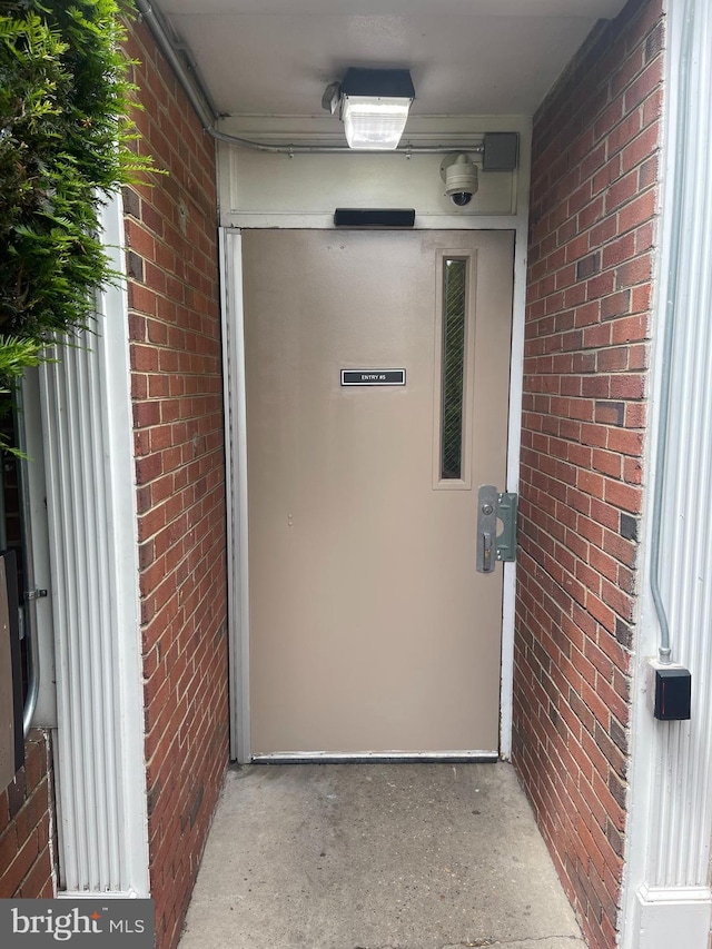 doorway to property featuring brick siding and a security system