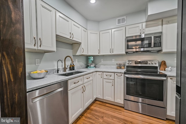 2501 Calvert St NW Unit 306, Washington, DC 20008 - kitchen with stainless steel appliances, a sink, light wood-style flooring, light stone counters, and white cabinetry