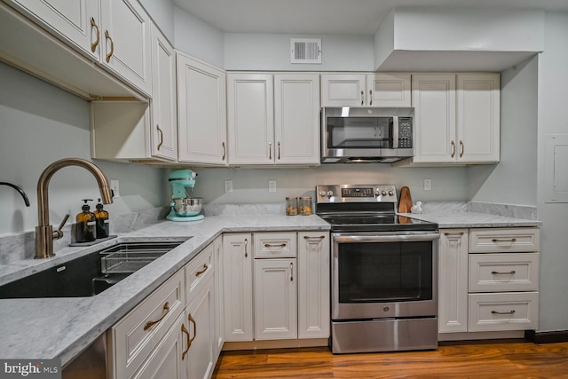 2501 Calvert St NW Unit 306, Washington, DC 20008 - kitchen with stainless steel appliances, a sink, white cabinets, dark wood-style floors, and light stone counters