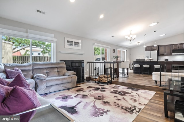 370 Juniper Ct, Herndon, VA 20170 - living area with a chandelier, healthy amount of natural light, vaulted ceiling, wood finished floors, and a fireplace with flush hearth