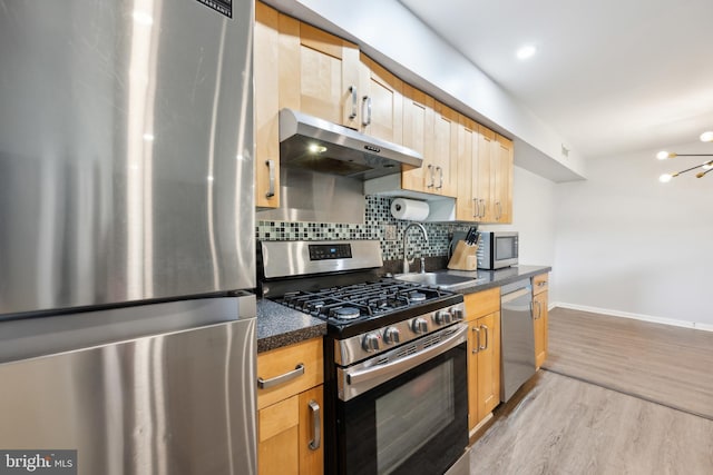 kitchen featuring stainless steel appliances, under cabinet range hood, a sink, dark countertops, and tasteful backsplash