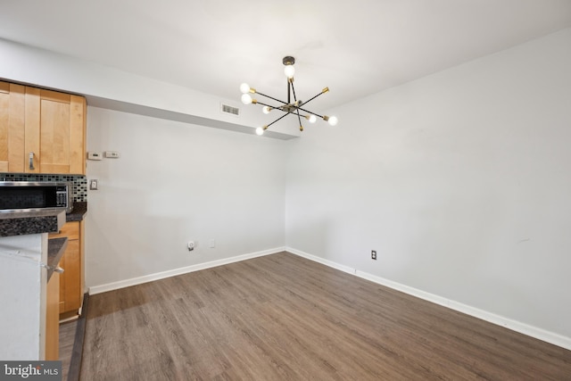unfurnished dining area with a chandelier, dark wood finished floors, and baseboards