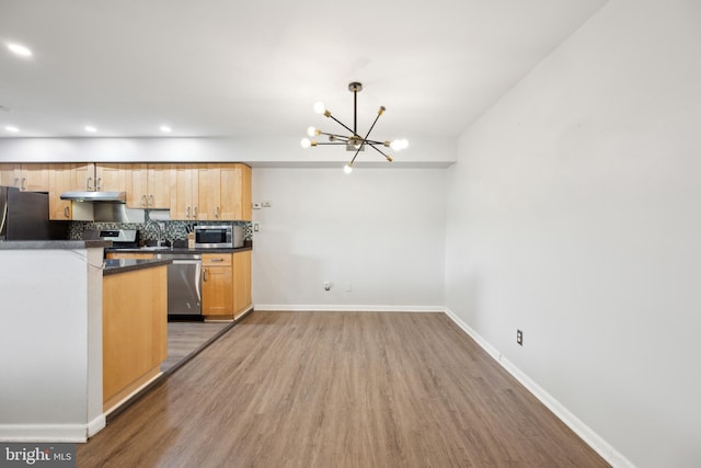 kitchen featuring appliances with stainless steel finishes, dark countertops, a chandelier, light wood-style floors, and under cabinet range hood