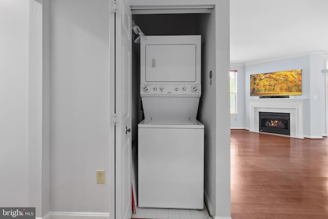 4950 Brenman Park Dr Unit 301, Alexandria, VA 22304 - washroom featuring estacked washer and dryer, baseboards, wood finished floors, ornamental molding, and a fireplace with flush hearth
