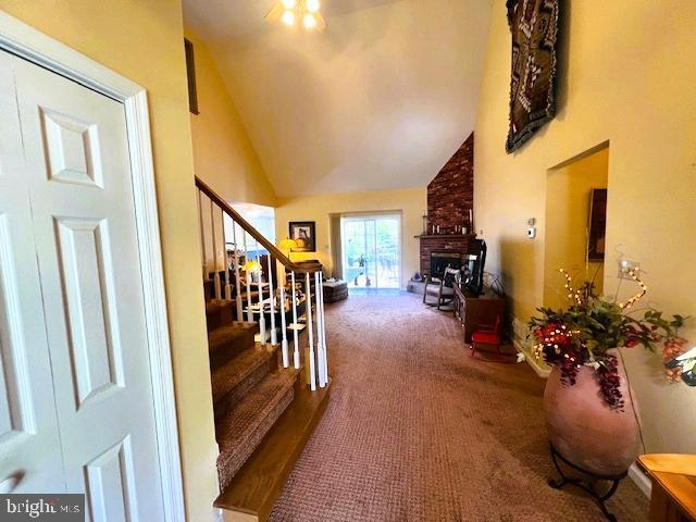 carpeted entryway with high vaulted ceiling, stairs, and a fireplace