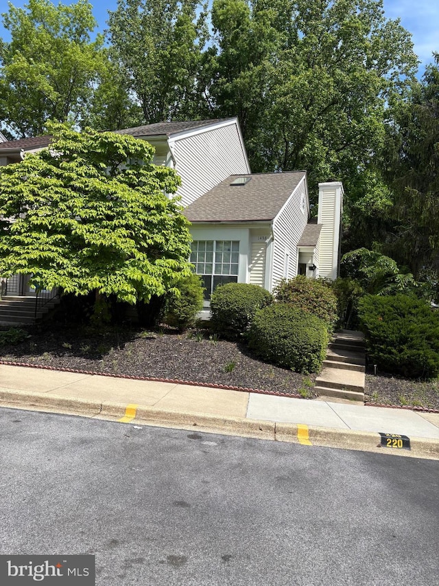 view of property hidden behind natural elements with a chimney and a shingled roof