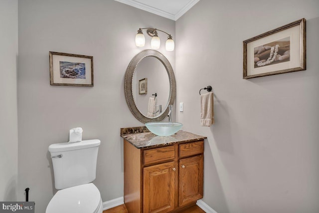 half bathroom with ornamental molding, toilet, vanity, and baseboards