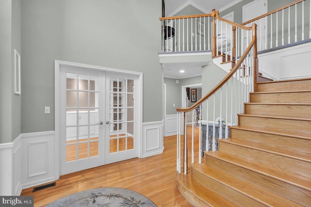 foyer with a high ceiling, french doors, wood finished floors, wainscoting, and stairway