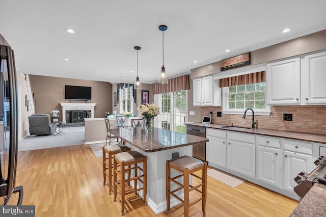 kitchen featuring dishwasher, a sink, light wood-style flooring, dark stone counters, and recessed lighting