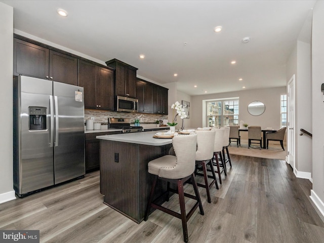 14716 Spring Haven Ln, Laurel, MD 20707 - kitchen featuring appliances with stainless steel finishes, a kitchen island with sink, light countertops, dark brown cabinets, and decorative backsplash