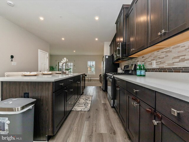 14716 Spring Haven Ln, Laurel, MD 20707 - kitchen with stainless steel gas stove, a kitchen island with sink, light wood-style floors, backsplash, and light countertops