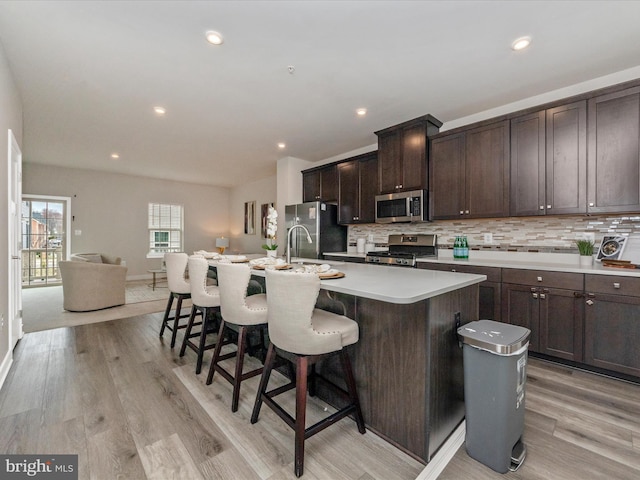 14716 Spring Haven Ln, Laurel, MD 20707 - kitchen with appliances with stainless steel finishes, dark brown cabinetry, a kitchen island with sink, a kitchen bar, and decorative backsplash