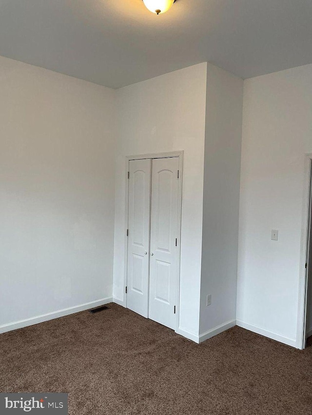 unfurnished bedroom with dark colored carpet, baseboards, and a closet