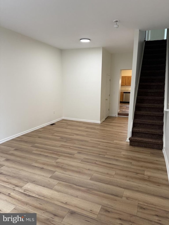 unfurnished living room featuring stairs, light wood-style flooring, and baseboards