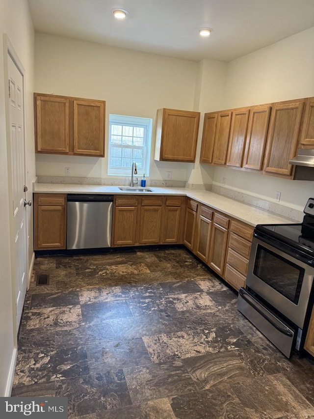 kitchen featuring stainless steel appliances, a sink, under cabinet range hood, brown cabinetry, and light countertops