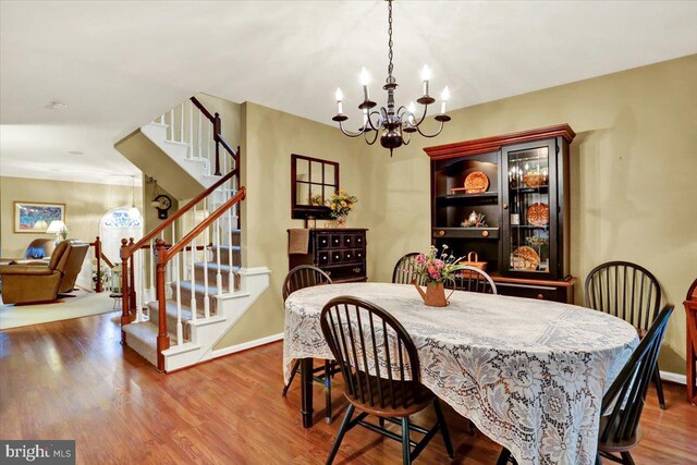 dining space with a chandelier, stairway, baseboards, and wood finished floors