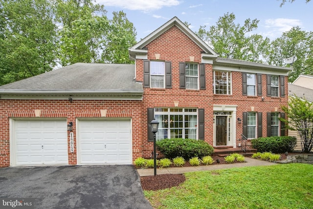 colonial house featuring a garage, asphalt driveway, brick siding, and a shingled roof